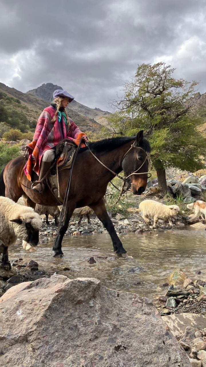 Jinete con poncho vadeando un arroyo junto al arreo